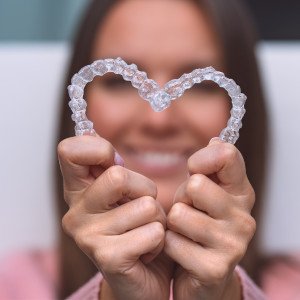 Woman holding Invisalign aligners in the shape of a heart 