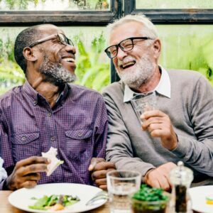 two older men smiling, laughing, and eating together