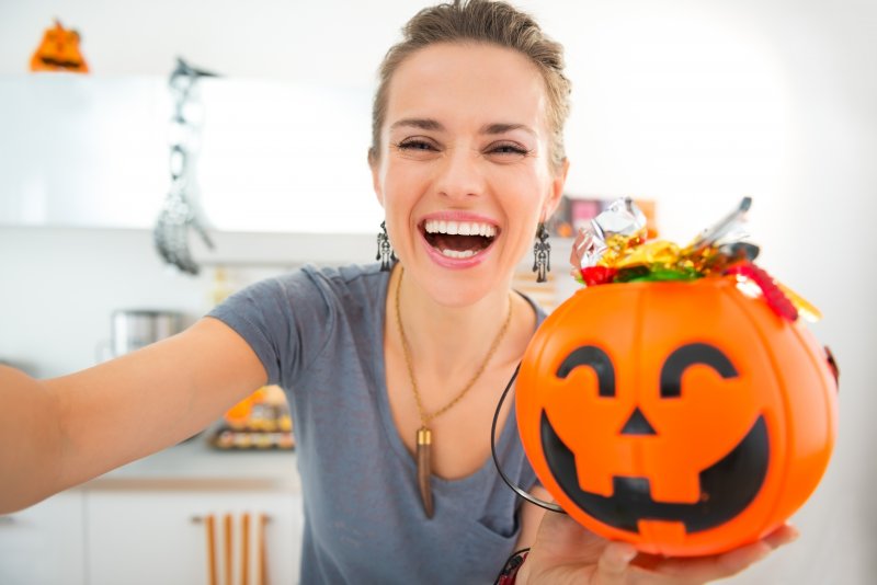 smiling woman taking a selfie with a candy-filled pumpkin bucket